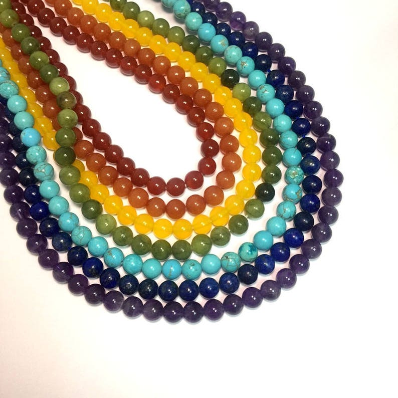 May include: A rainbow of round gemstone beads strung together in a necklace. The beads are purple, blue, turquoise, green, yellow, orange, and red.