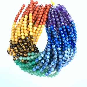 May include: A set of seven strands of gemstone beads in rainbow colors. The beads are round and faceted. The colors are red, orange, yellow, green, blue, indigo, and violet.