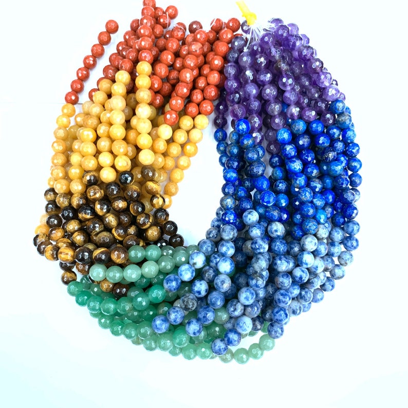 May include: A set of seven strands of gemstone beads in rainbow colors. The beads are round and faceted. The colors are red, orange, yellow, green, blue, indigo, and violet.