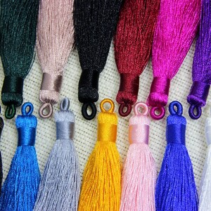 May include: Assortment of 12 silk tassels in various colors, including black, blue, green, pink, red, white, and yellow. The tassels are approximately 2 inches long and have a loop at the top for easy attachment.