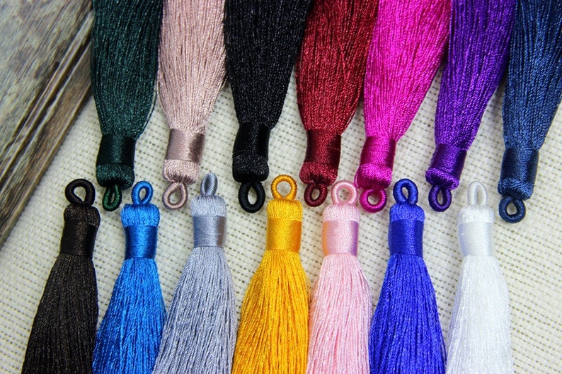 May include: Assortment of 12 silk tassels in various colors, including black, blue, green, pink, red, white, and yellow. The tassels are approximately 2 inches long and have a loop at the top for easy attachment.