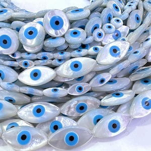 May include: A strand of white oval-shaped beads with blue evil eye designs. The beads are made of mother of pearl and have a iridescent sheen.