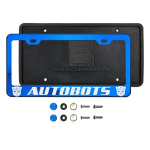 May include: A blue metallic license plate frame featuring the word AUTOBOTS in white lettering, flanked by two Autobot logos. The frame is positioned over a black rectangular backing plate with a textured surface. Includes two sets of mounting hardware.