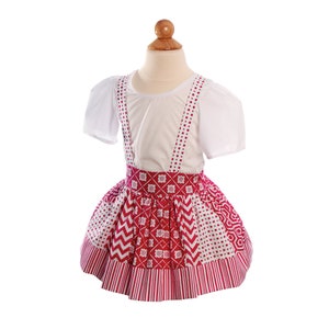 May include: A white short-sleeved shirt with a red and white patterned skirt with suspenders. The skirt has a variety of geometric patterns in red and white.