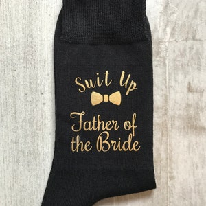 May include: Black socks with gold lettering that says "Suit Up" with a bow tie graphic and "Father of the Bride".
