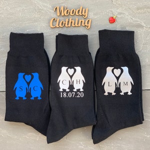 May include: Three pairs of black socks with penguin designs. The penguins are holding hearts with initials and a wedding date. The socks are a fun and unique gift for a couple.
