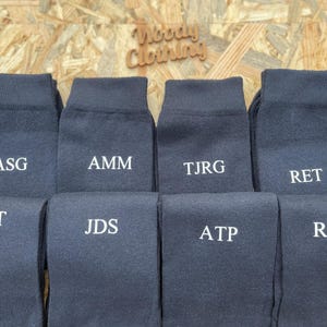 Puede incluir: Diez pares de calcetines de color gris oscuro con iniciales bordadas en blanco. Las iniciales son: ASG, AMM, TJRG, RET, MET, JDS, ATP, RAS.