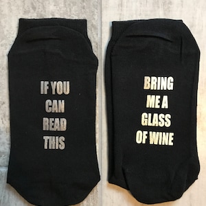 May include: A pair of black socks with white text. One sock says "If you can read this" and the other sock says "Bring me a glass of wine".