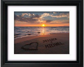May include: A framed photograph of a beach sunset with the words "Jessica + Michael" written in the sand, along with a heart drawn in the sand.