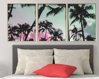 Op de afbeelding: Een set van drie ingelijste prints met een silhouet van palmbomen tegen een pastelroze en blauwe lucht.