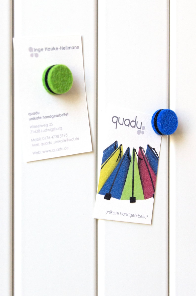 May include: Two business cards with the text "quadu unikate handgearbeitet" and a logo of colorful tents. One card has a green felt magnet and the other has a blue felt magnet.