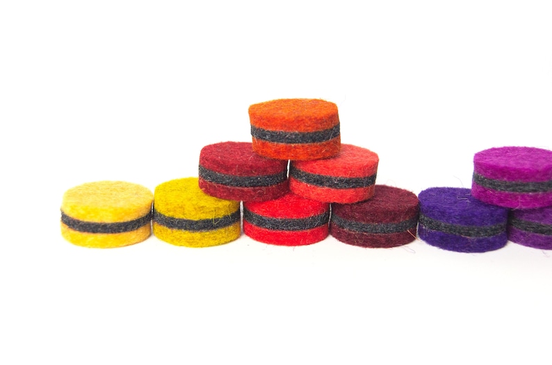 May include: A set of nine felt circles in various colors, including yellow, orange, red, purple, and burgundy. Each circle has a black band around the middle.
