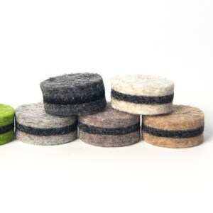 May include: A set of six felt furniture pads in various colors, including green, gray, beige, and brown. Each pad has a black felt ring around the edge.