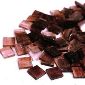May include: A pile of small, square, brown glass mosaic tiles. The tiles have a translucent, iridescent quality.