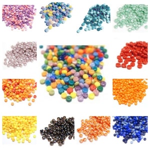 Könnte beinhalten: Sortiment kleiner, runder Glasfliesen in verschiedenen Farben, darunter Lila, Blau, Grün, Grau, Rot, Orange, Gelb, Schwarz und Braun. Die Fliesen sind auf einem weißen Hintergrund verstreut.