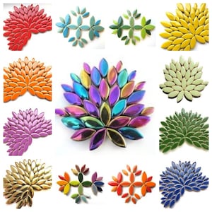 Op de afbeelding: Assortiment van keramische mozaïektegels in bladvorm in verschillende kleuren, waaronder rood, oranje, geel, groen, blauw, paars, goud en iriserend. De tegels zijn in een cirkelvormig patroon gerangschikt.