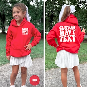 Puede incluir: Una sudadera roja con el texto "CUSTOM WAVY TEXT" en blanco en la parte delantera y trasera. Se combina con una falda plisada blanca. Un c&iacute;rculo rojo con la palabra "RED" est&aacute; en la parte inferior.