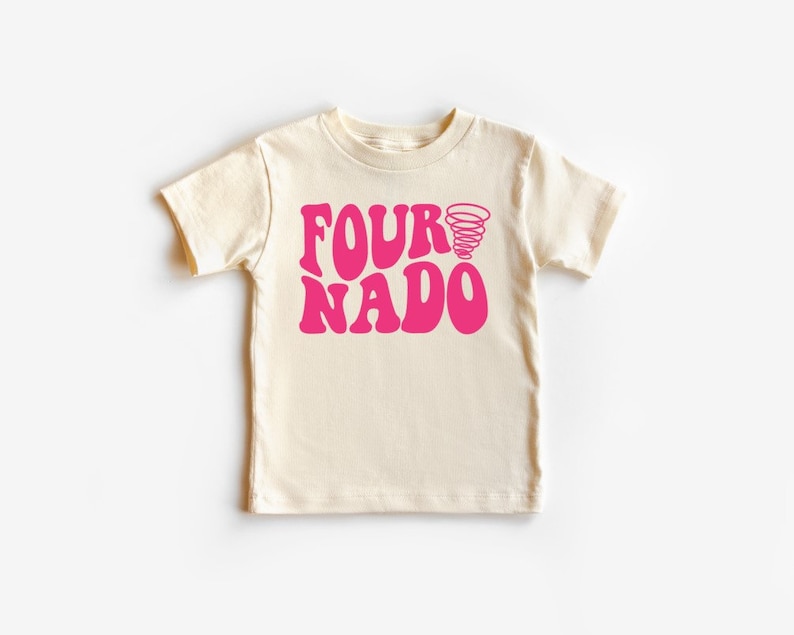 Pu&ograve; includere: Una maglietta color crema con una grafica rosa che dice "Fournado" con un design a spirale rosa.
