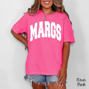 May include: Neon pink t-shirt with the word "MARGS" in large white block letters across the chest. The shirt is a vibrant, solid color and has short sleeves. The text "Neon Pink" is in the bottom right corner.