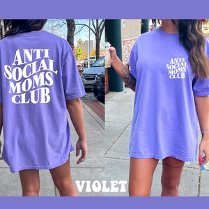 May include: A purple oversized t-shirt with the text "Anti Social Moms Club" in white. The shirt is made of a soft, comfortable material and has a relaxed fit.