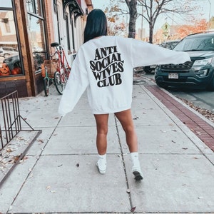 Puede incluir: Sudadera blanca con texto negro en la espalda que dice "Anti Social Wives Club".