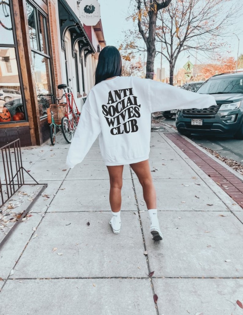 Puede incluir: Sudadera blanca con texto negro en la espalda que dice "Anti Social Wives Club".