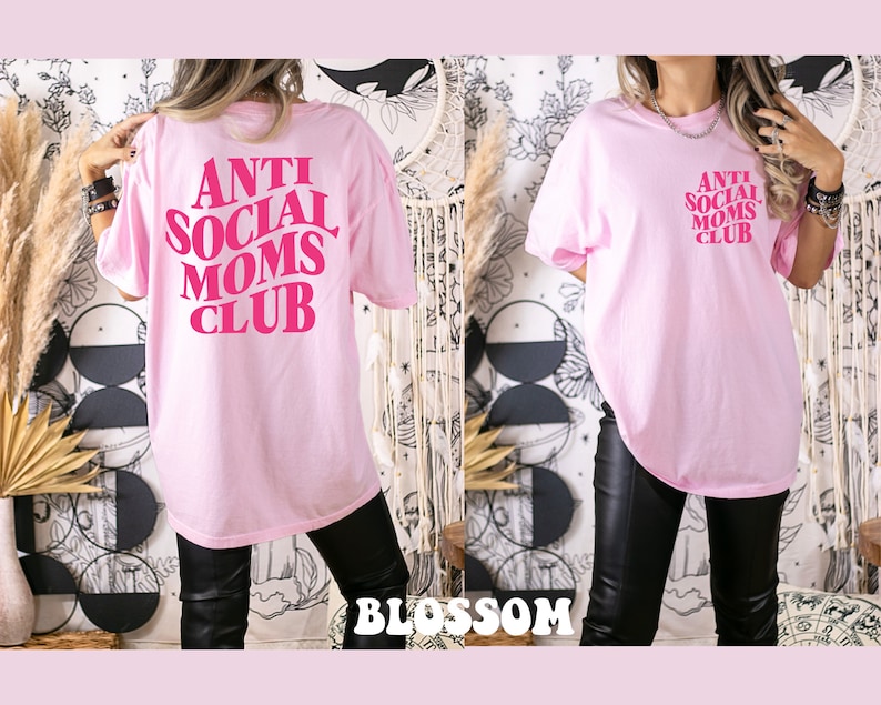 May include: Pink oversized t-shirt with the text "Anti Social Moms Club" in pink lettering. The shirt is being worn by a person with black pants.