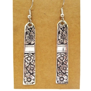 May include: A pair of silver dangle earrings with a floral design. The earrings are long and rectangular in shape, with a silver hook.