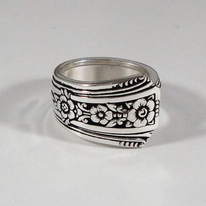 May include: A silver ring with a floral design. The ring is made from a recycled spoon and features three flowers with intricate details.