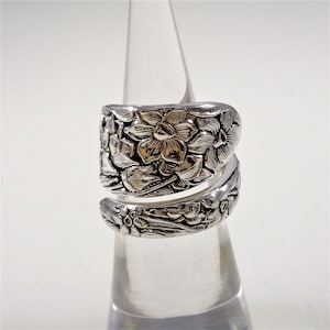 May include: A silver ring with a floral design. The ring is made from a spoon and is a unique piece of jewelry.