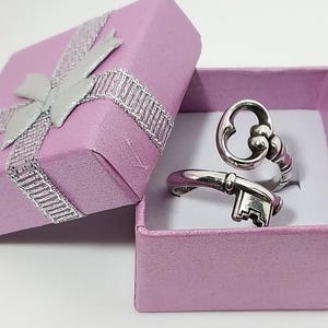 May include: A silver key-shaped ring in a pink gift box with a silver ribbon.
