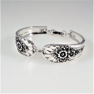 May include: A silver bracelet made from a vintage spoon with floral designs. The bracelet is connected with a silver chain.