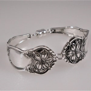 May include: A silver bracelet made from a repurposed spoon with a floral design. The bracelet has a magnetic clasp.