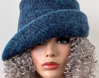 Puede incluir: Un sombrero de fieltro azul con un ala ancha, inclinado hacia un lado, usado por un maniquí con cabello rizado plateado.
