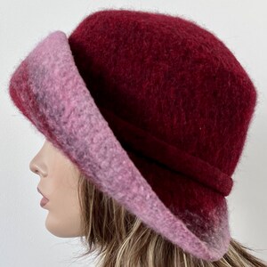 May include: A burgundy and pink wool felt hat with a wide brim. The hat is soft and has a slouchy look.