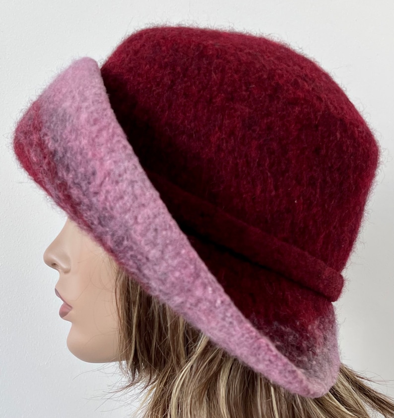 May include: A burgundy and pink wool felt hat with a wide brim. The hat is soft and has a slouchy look.
