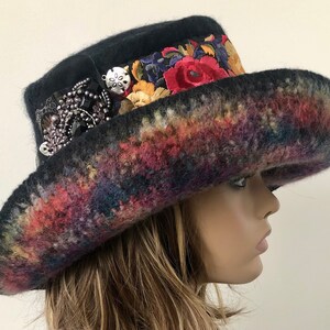 May include: A black felt hat with a wide brim and a colorful, embroidered band. The hat is decorated with a large, silver-toned brooch.