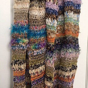 May include: A multi-colored crocheted scarf with fringe. The scarf is made with a variety of textures and colors, including brown, green, blue, orange, and purple.