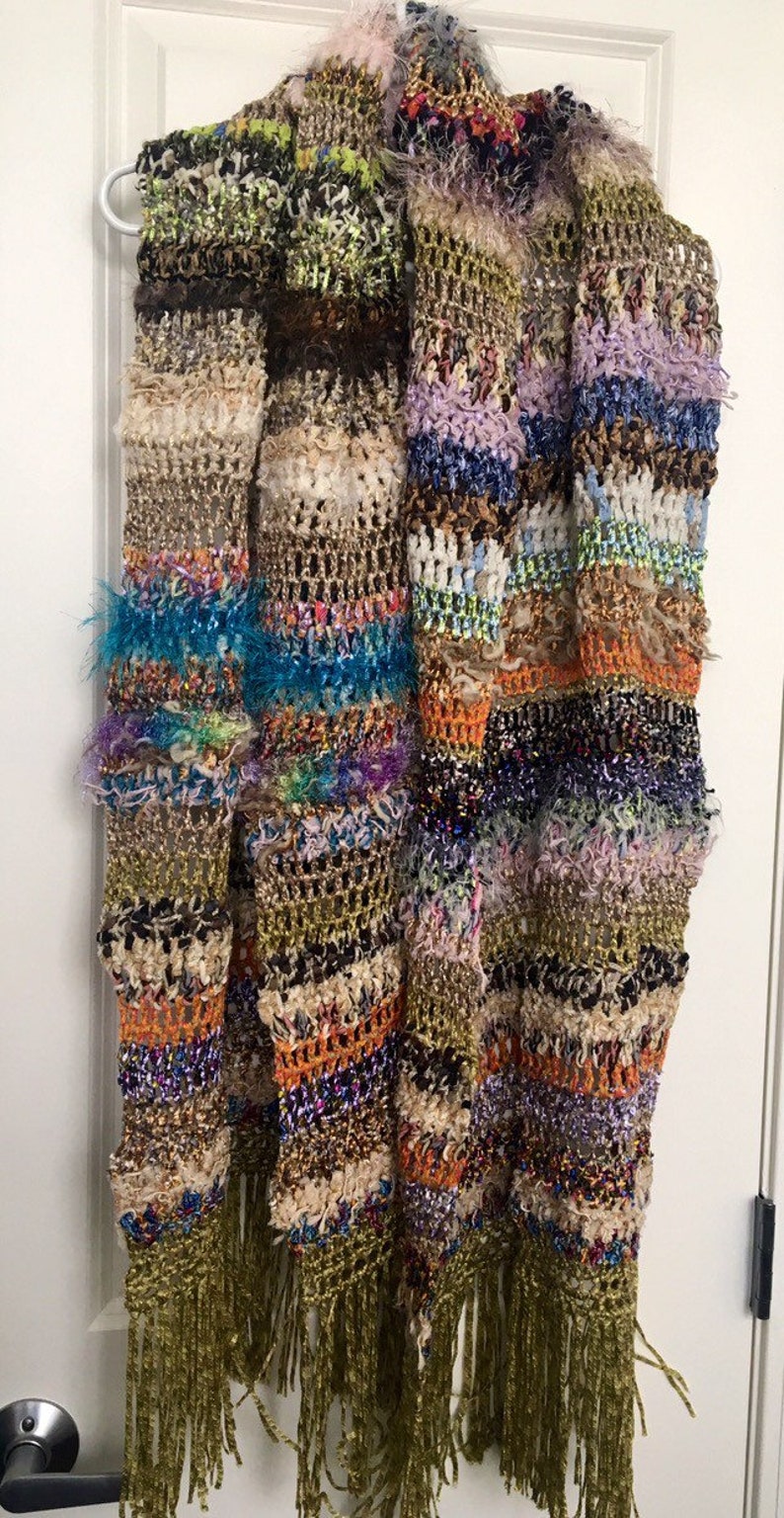 May include: A multi-colored crocheted scarf with fringe. The scarf is made with a variety of textures and colors, including brown, green, blue, orange, and purple.