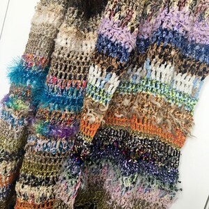May include: A multi-colored crocheted cardigan with a textured, fuzzy look. The cardigan features stripes of various colors, including brown, blue, green, orange, and purple.
