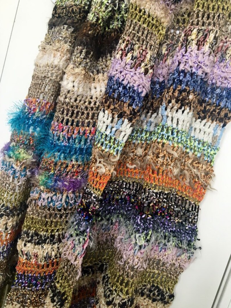May include: A multi-colored crocheted cardigan with a textured, fuzzy look. The cardigan features stripes of various colors, including brown, blue, green, orange, and purple.