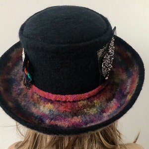 May include: A black felt hat with a wide brim and a colorful, tie-dye pattern on the underside of the brim. The hat has a decorative band with a pink trim and silver embellishments.