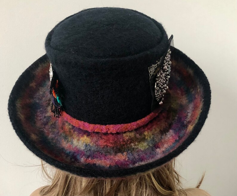 May include: A black felt hat with a wide brim and a colorful, tie-dye pattern on the underside of the brim. The hat has a decorative band with a pink trim and silver embellishments.