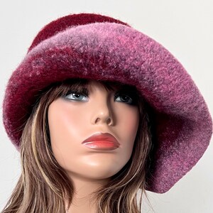 May include: A pink and burgundy wool felt hat with a wide brim. The hat is slouched and has a soft, fuzzy texture.