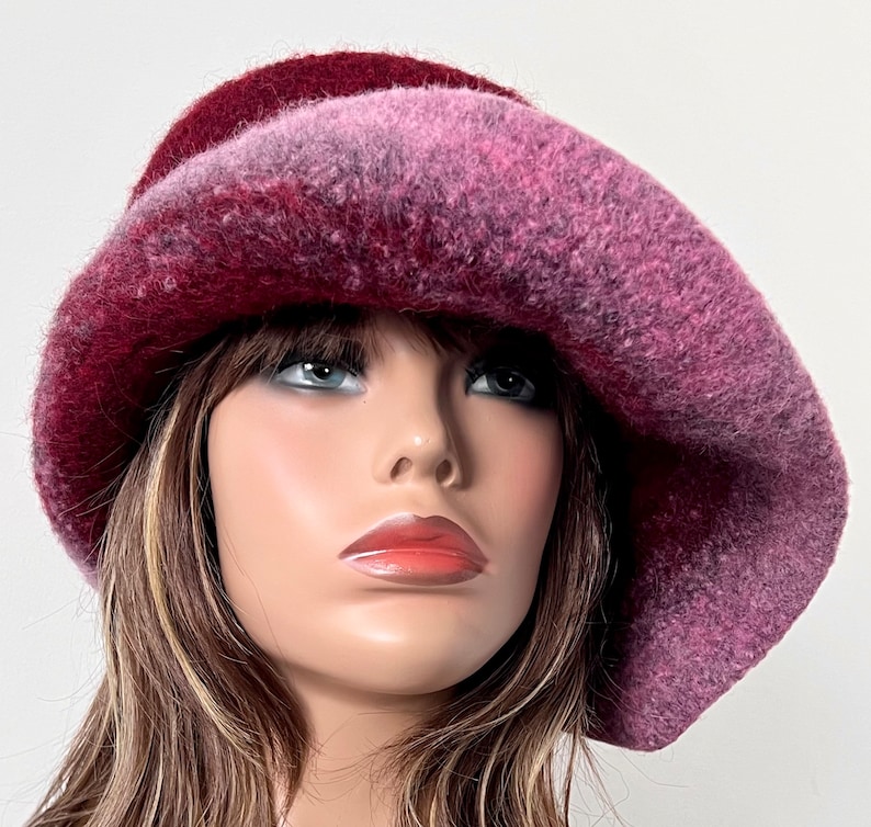 May include: A pink and burgundy wool felt hat with a wide brim. The hat is slouched and has a soft, fuzzy texture.