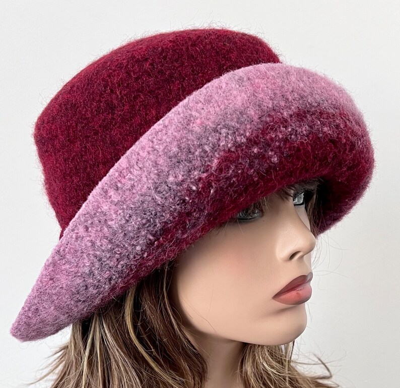 May include: A burgundy felt hat with a wide brim, featuring a gradient of pink and purple hues.
