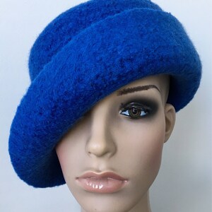 May include: A bright blue felt hat with a wide brim, angled to the side. The hat is made of a soft, fuzzy material.