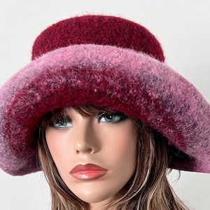 May include: A wide-brimmed hat with a gradient of pink and burgundy colors. The hat is made of a soft, fuzzy material.