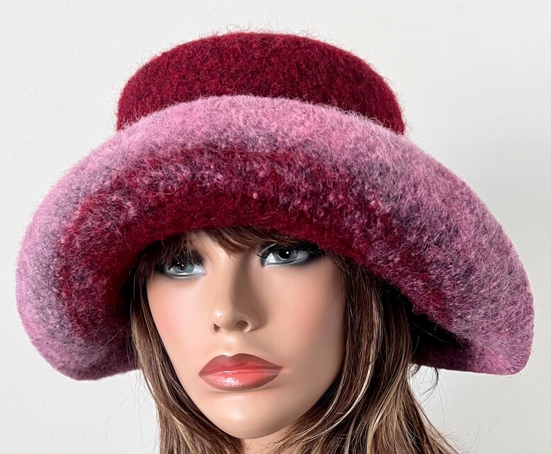 May include: A wide-brimmed hat with a gradient of pink and burgundy colors. The hat is made of a soft, fuzzy material.