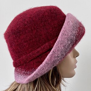 May include: A burgundy and pink wool felt hat with a wide brim. The hat is soft and fluffy, and the brim is turned up on one side.